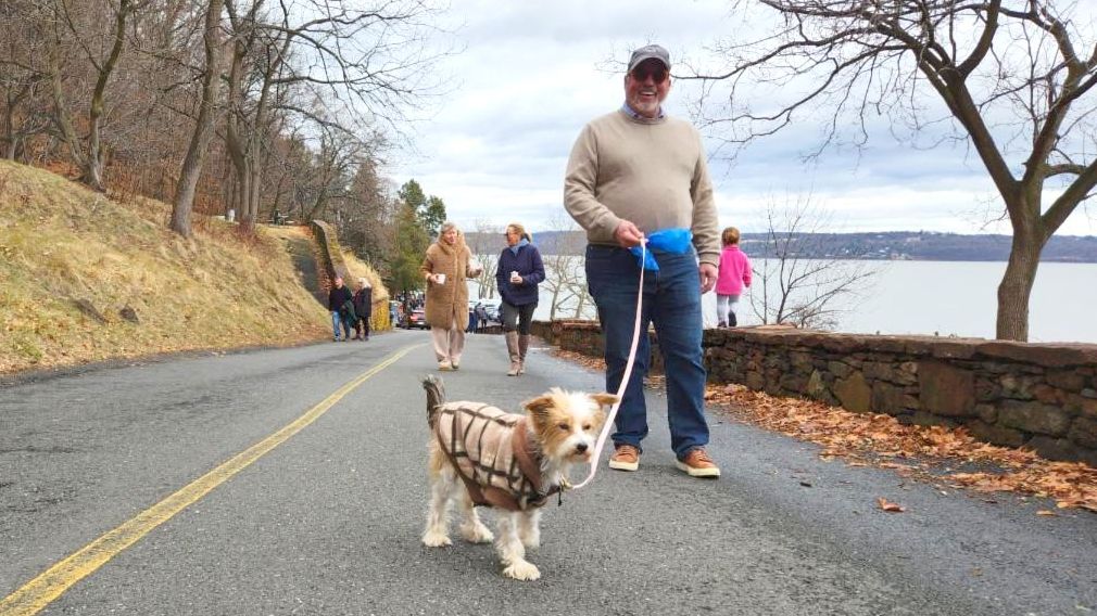 A festival attendee walking up the road from the Nyack Beach Bathhouse with their dog. The Hudson River can be seen in the background.