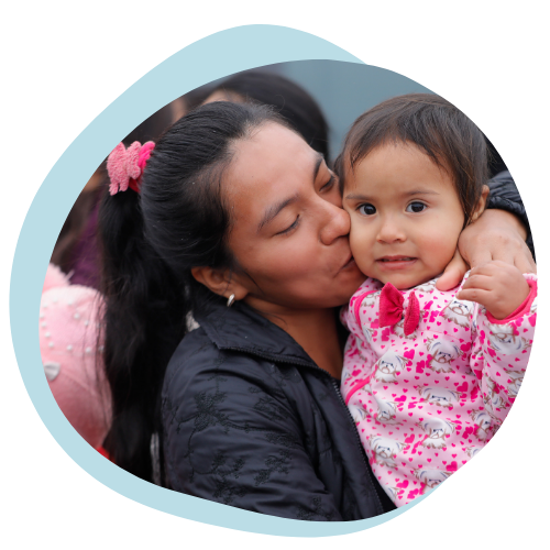 A Native American woman holds and kisses her baby on the cheek. 