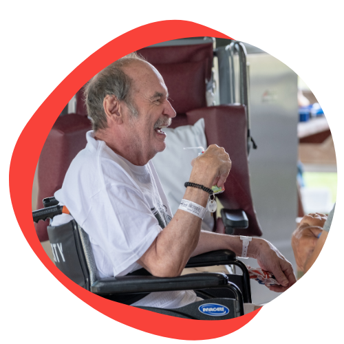 An older white man laughing. He is leaving the hospital in a wheelchair. 