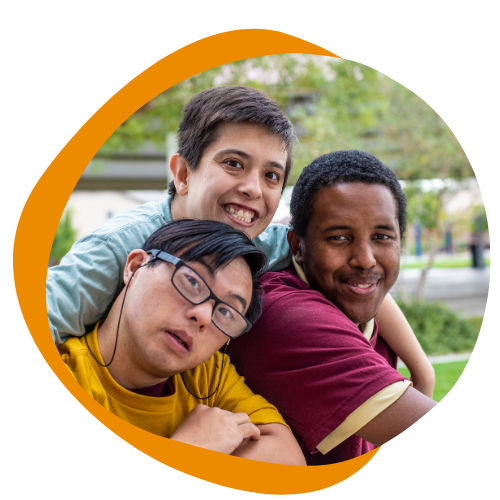A diverse group of young disabled men poses for a picture together. They are all wearing brightly colored shirts and smiling at the camera. 