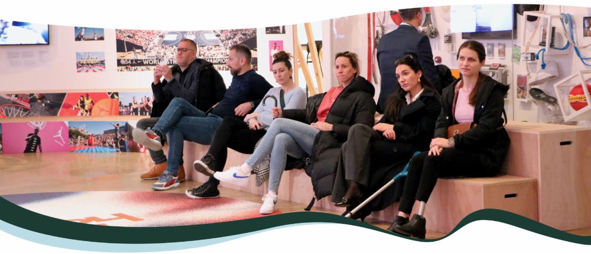 A group of six people sits and watches something. They are a diverse group of people with visible and non-visible disabilities. 