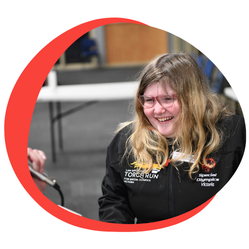 A young white girl in a wheelchair with glasses smiling.