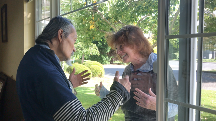 a man and women gesture kindly to each other through a window 