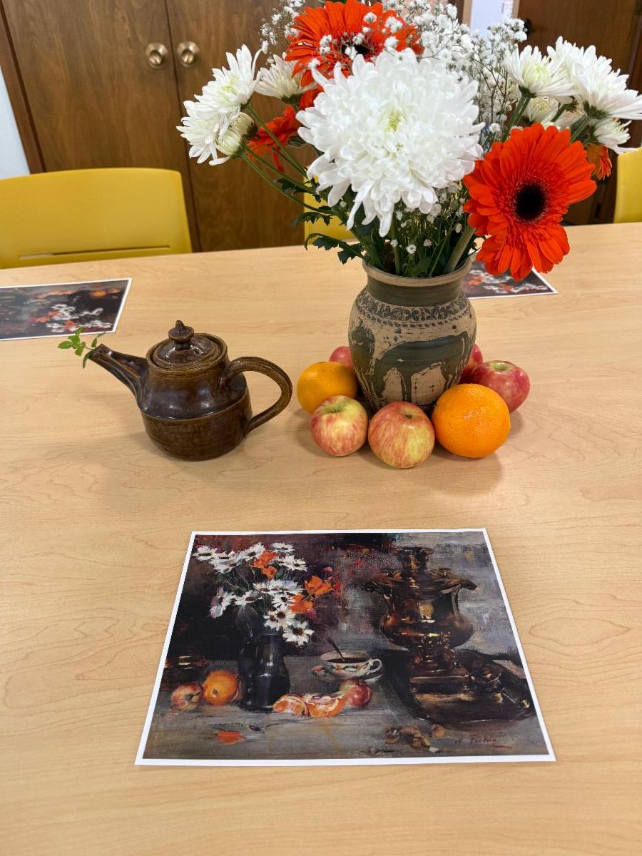 A tea pot, fruits, and vase of white and orange flowers on a table