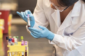 A female in a lab coat examines a test tube of blood