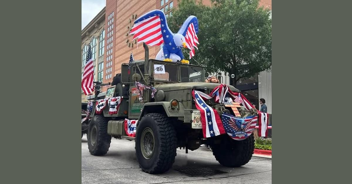 Photo of military jeep vehicle covered in 4th of July decorations one of which is a large Christian cross painted with the American flag on the front of the vehicle