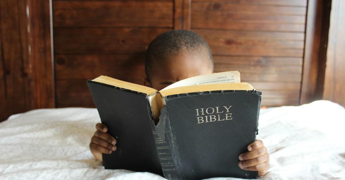 Small child reading bible that's bigger than they are