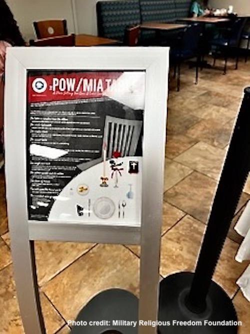 Poster next to POW MIA table showing Bible with large cross on it 