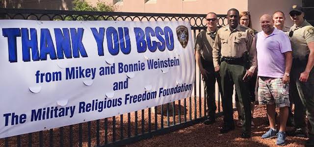 Mikey and Bonnie Weinstein with sheriff's deputies next to big Thank you sign from MRFF
