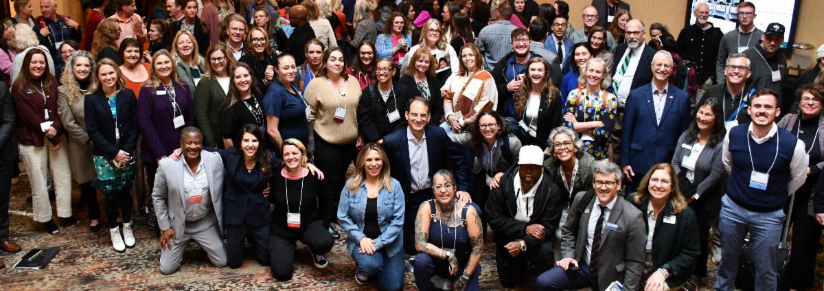 Group of 200+ individuals in business attire smiling for a photo on the floor of a conference center.
