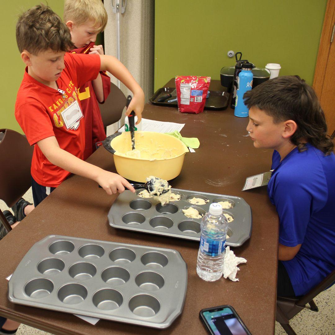 youth in kitchen filling cupcake tins with batter