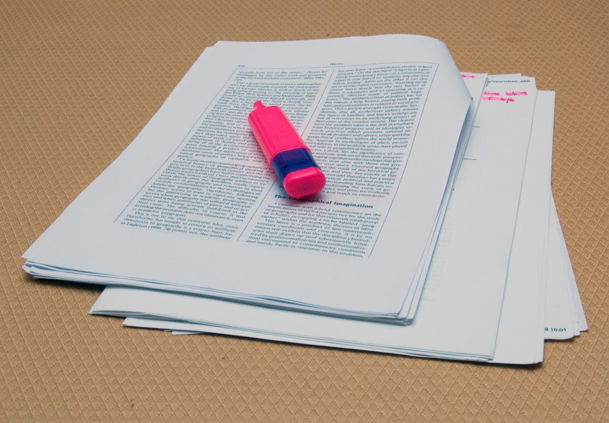 Photo of academic essay with a pink highlighter sitting on top of the pages