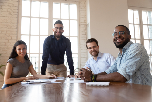 Portrait of happy millennial multiethnic work team sit at office desk brainstorming at meeting looking at camera_ successful smiling diverse businesspeople posing in boardroom gather at briefing