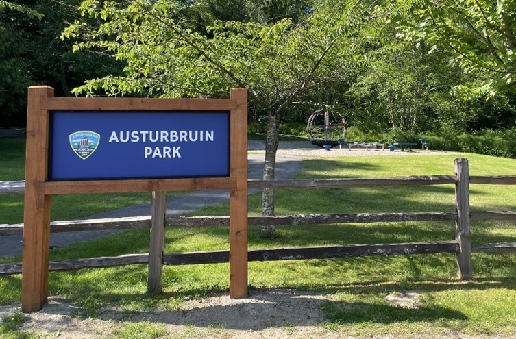 Blue background with white writing attached by wooden posts and framed with wood show the new signage for Austurbruin Park.