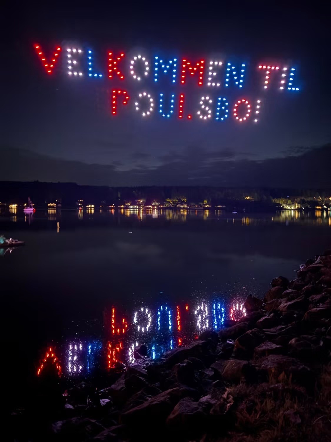 Red, white and blue Velkommen Til Poulsbo sign in the night sky made by drones.