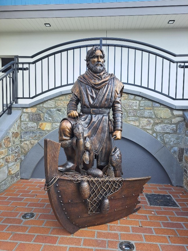 Art sculpture of the fisherman standing in front of a boat with fish he caught.
