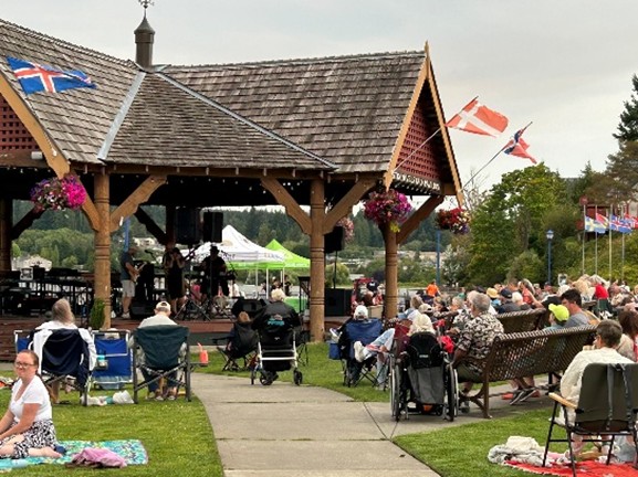 People sitting in lawn chairs and benches listening to a summer concert at the bay.