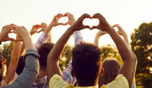 Happy adult diverse multiethnic people raise hands up in air_ do heart shaped gestures_ share good vibes_ hope for peaceful future_ send kind wishes to universe. Outdoor outside back view group shot