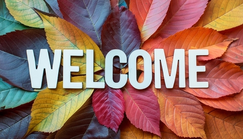 A welcome sign made of white letters on a background of colorful autumn leaves in various shades of red_ orange_ yellow_ and green.
