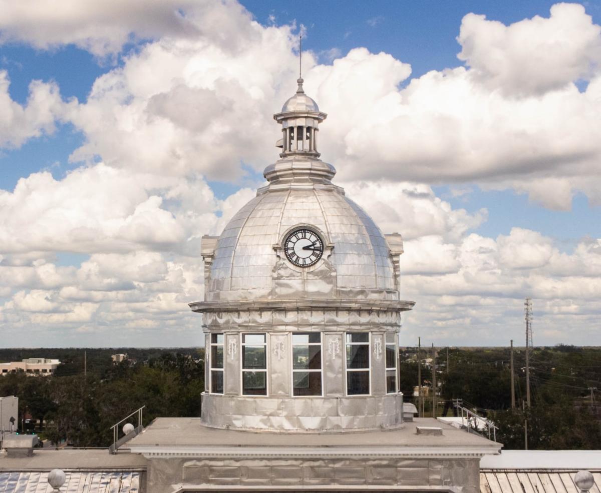 A silver domed clock tower rises above a small downtown area and a partly cloudy sky.