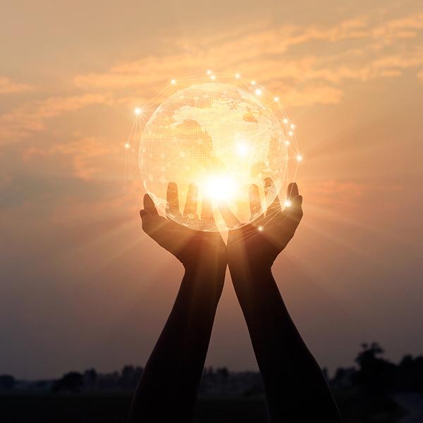 Hands holding up a digital globe in front of the sunset