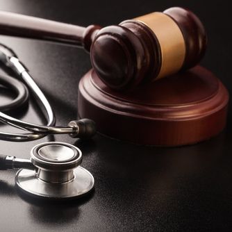 Judge's gavel sitting on a dark surface next to a stethoscope