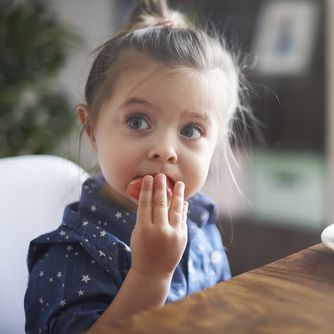 Young child sitting at a table eating vegetables