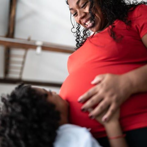 A Black-presenting pregnant person smiling down at a child holding her stomach