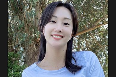 Ye Ji Kim, a smiling Korean-American woman with shoulder length dark hair wearing a light blue top standing in front of a tree