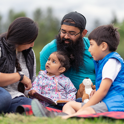 Indigenous family sitting and reading together in an open green space
