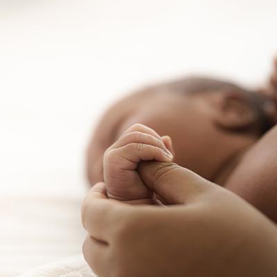 Black-presenting baby holding hands with what appears to be an adult