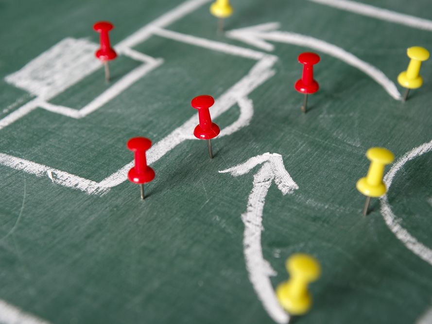 Red and yellow push pins on a green board that represent a soccer play
