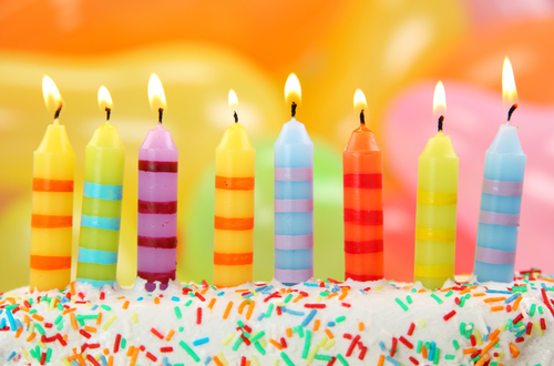 Eight colorfully stripped and lit birthday candles on white surface with sprinkles