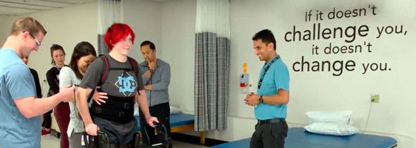 Patient using a mobility device while walking is surrounded by their physio, clinician, and research care team.