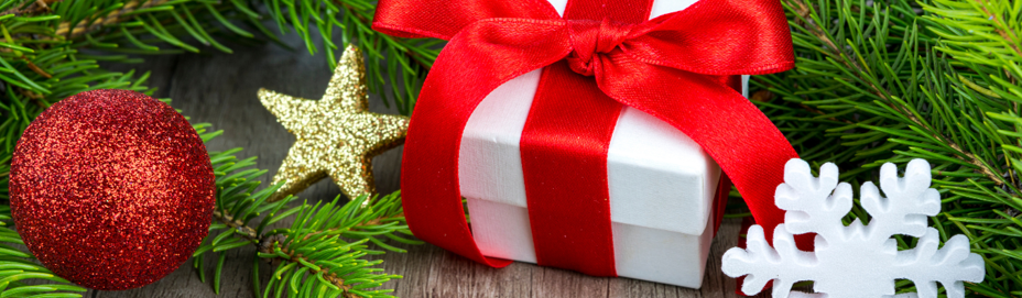 Season greetings. Ornaments and a present rest on a table surrounded by pine tree branches.