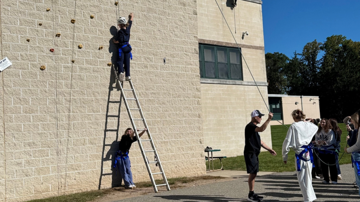 Student in Ramapo High School Phys Ed class begins climbing the building's exterior with safety harness