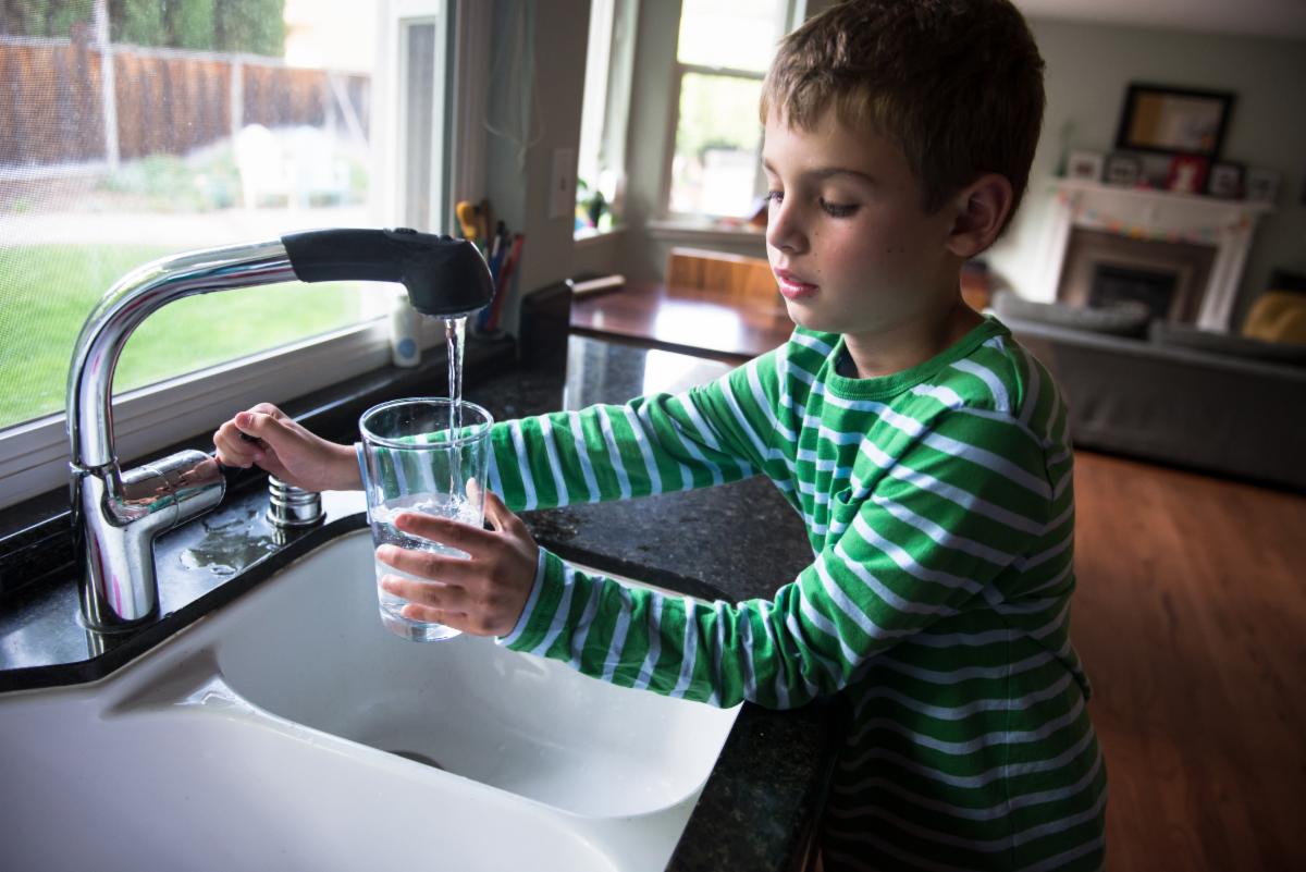 Child filling up glass of water at the sink. 