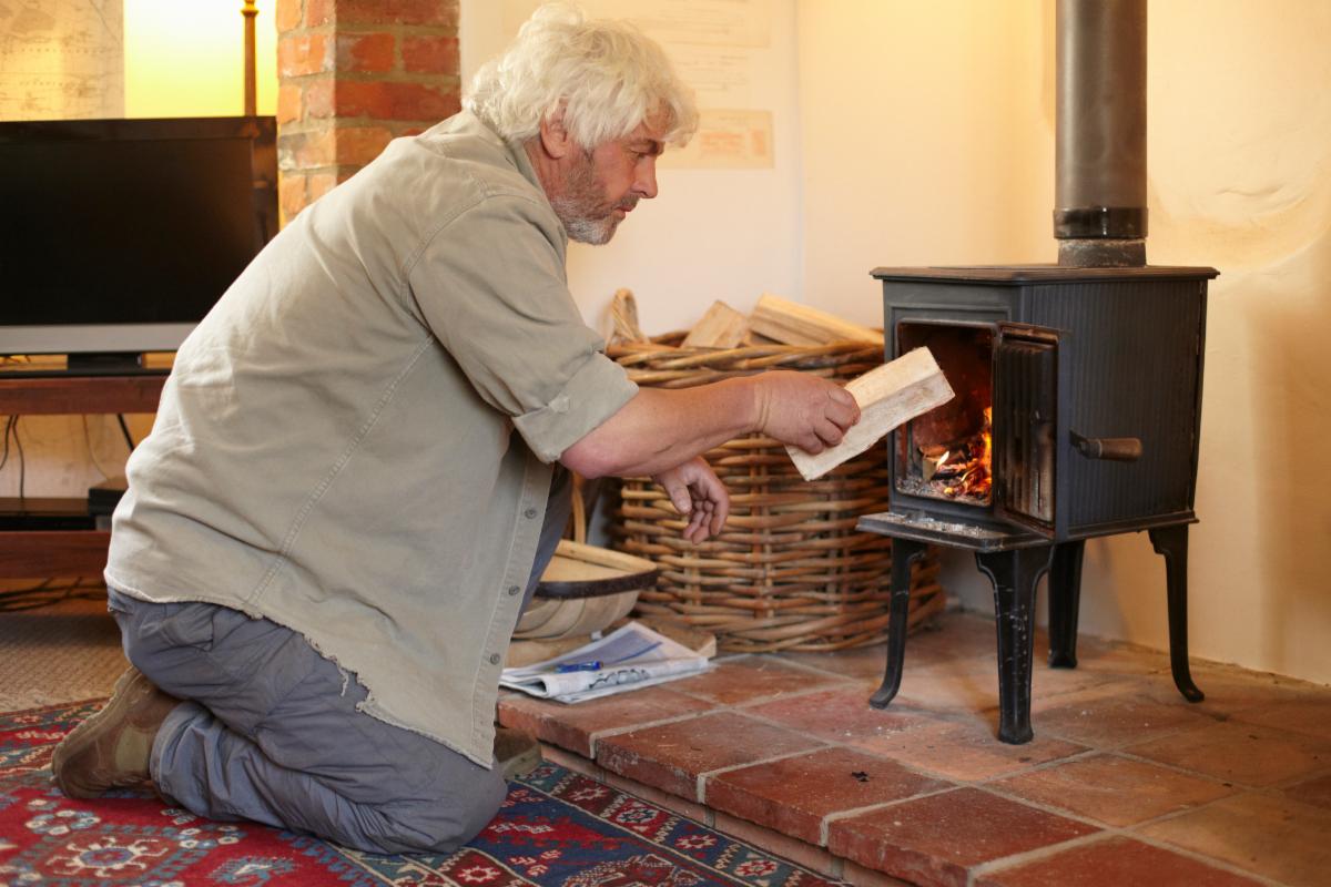 Person adding a log to a wood stove.