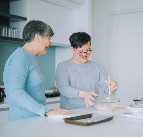 An Asian-American grandmother and her teenage grandson with a disability smile as they bake together