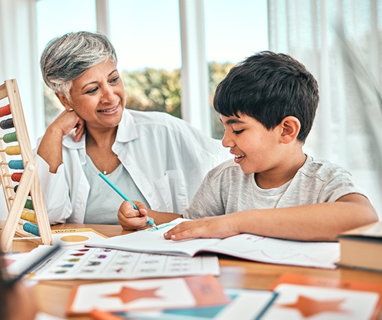 A grandmother smiling at her grandson, who is drawing at a desk