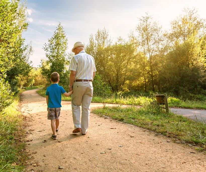 A white grandfather and grandson hold hands and walk along a path
