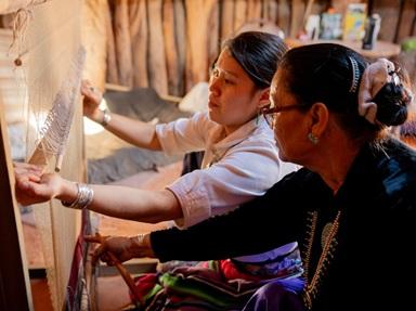 A Native grandmother helps her granddaughter use a loom to weave a traditional design