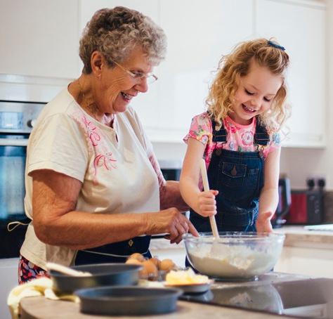 A white grandmother and her young granddaughter smile as they mix ingredients together in the kitchen
