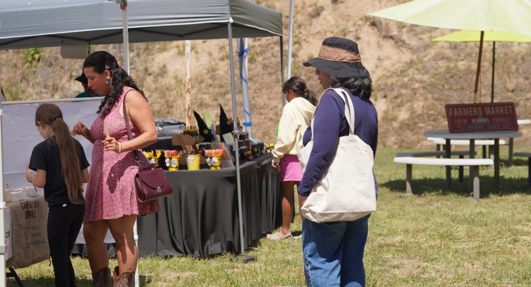 Visitors browse vendor booths during the first CA Hot Springs Capineros Farmers Market, with handmade goods and community booths visible beneath shaded tents.