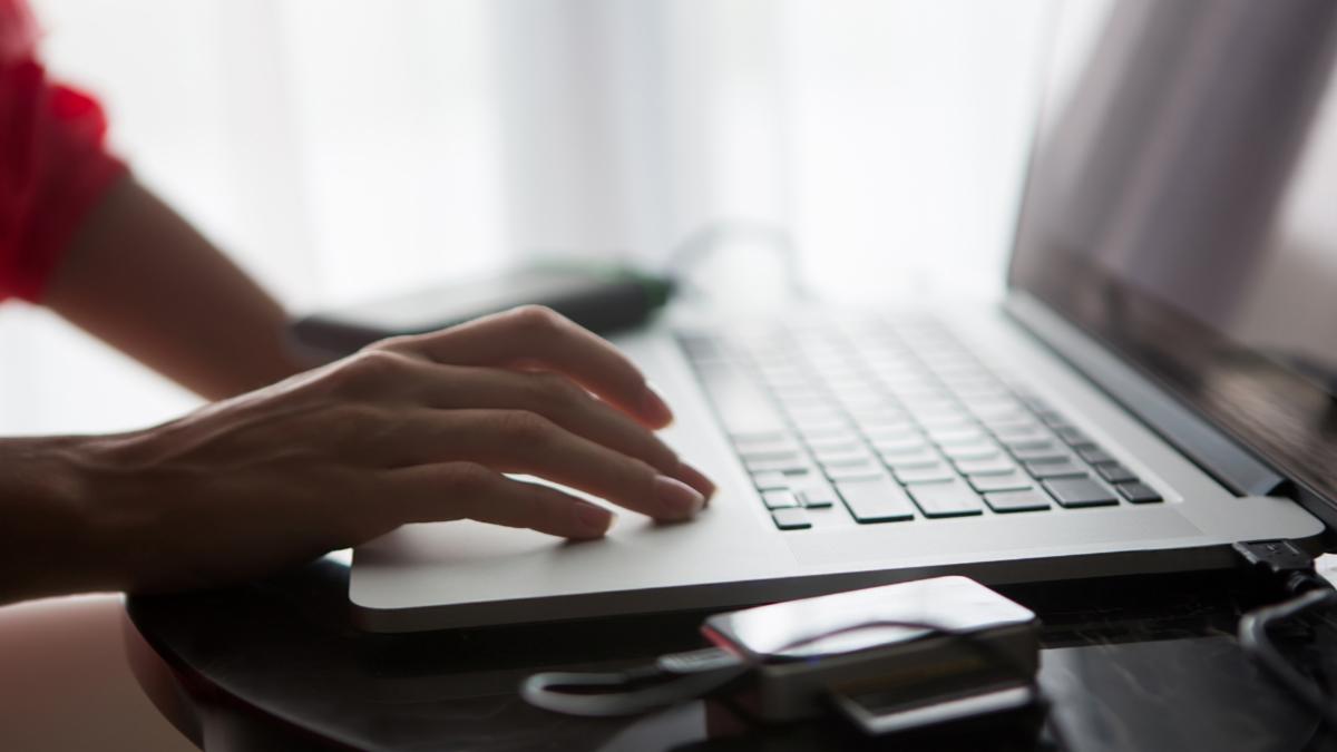 Close-up of a person using a laptop computer at a desk with a USB drive nearby.