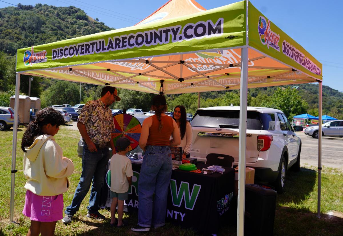 Visitors gather beneath a Discover Tulare County tent during the first CA Hot Springs Capineros Farmers Market, with community booths and vendor tents visible in the background.