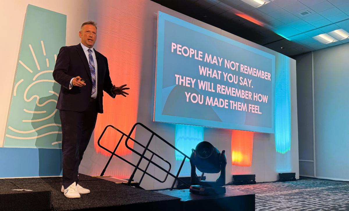 Joe Little of NBC 7 San Diego delivers a keynote presentation at CAPIO 2026 beside a screen displaying a message about the emotional impact of communication and storytelling.