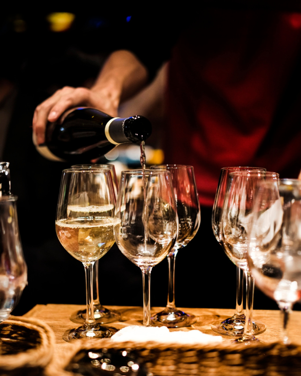 A server pours red wine into glowing wine glasses on a wooden table, creating an elegant, festive atmosphere at a wine tasting.