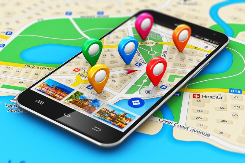 Macro view of modern black glossy touchscreen smartphone or mobile phone with wireless navigator map service internet application on screen and group of colorful destination pointer marker icons on city map with selective focus effect