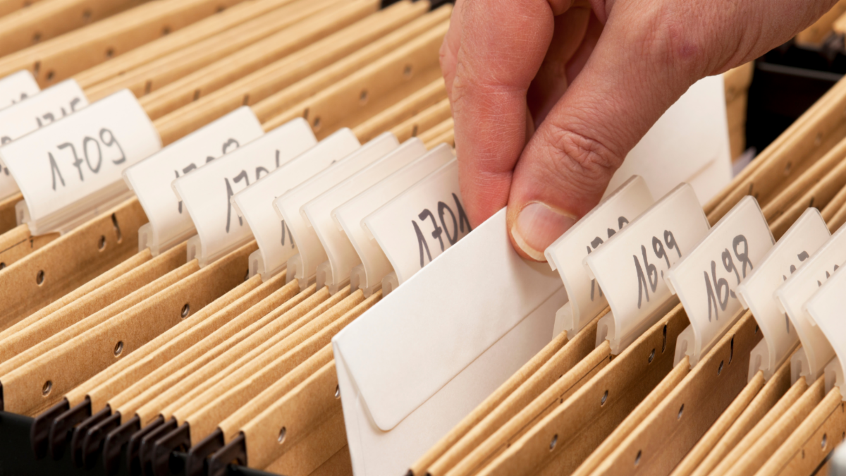 A hand pulling an envelope from a large collection of files.